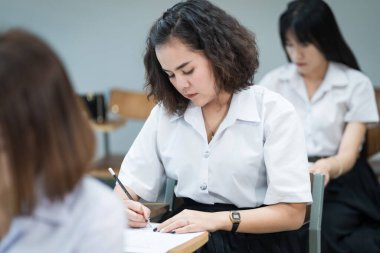 Genç üniversite öğrencilerinin seçici odak noktası ders koltuklarında oturup final sınavı yapmak ve sınav kağıdına cevap kağıtları yazmak. Üniformalı üniversite öğrencileri sınıfta..