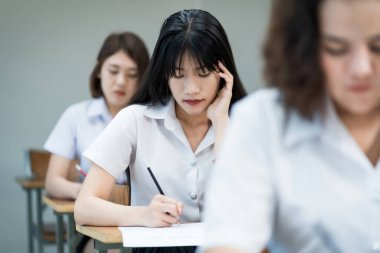 Sınıf başkanlığında oturan genç üniversite öğrencilerinin seçici odağı final sınavında sınav kağıdına cevap kağıdı yazıyorlar. Öğrenci üniformalı kız öğrenciler..