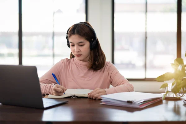 若いアジアの女の子の学生は オンライン時計を学習し 講師に耳を傾けるためにノートブック上の無線ヘッドフォンの書き込みを身に着けています 家庭でのビデオ通話電子学習を介してウェビナー 距離教育 — ストック写真