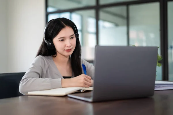 若いアジアの女の子の学生は オンライン時計を学習し 講師に耳を傾けるためにノートブック上の無線ヘッドフォンの書き込みを身に着けています 家庭でのビデオ通話電子学習を介してウェビナー 距離教育 — ストック写真