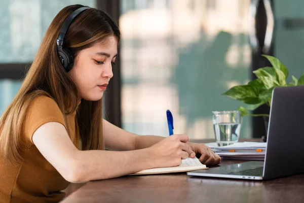 Joven Estudiante Asiática Lleva Auriculares Inalámbricos Concentrados Escribir Cuaderno Para —  Fotos de Stock