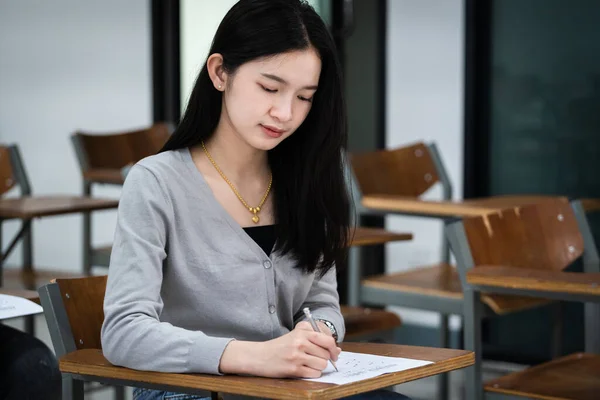 若い女子大生は教室で試験をすることに集中している 女子学生は真剣に教室での試験の練習を書きます — ストック写真