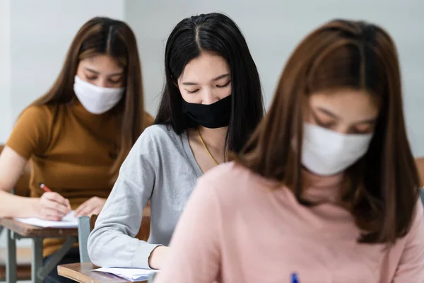 stock image Female teenager college students wears face mask and keep distance while studying in classroom and college campus to prevent COVID-19 pandemic