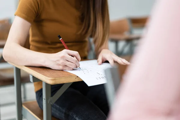 Close up of young female university students concentrate on doing examination in the classroom. Girl student writes the answer of the examinations on answer sheet in the classroom.