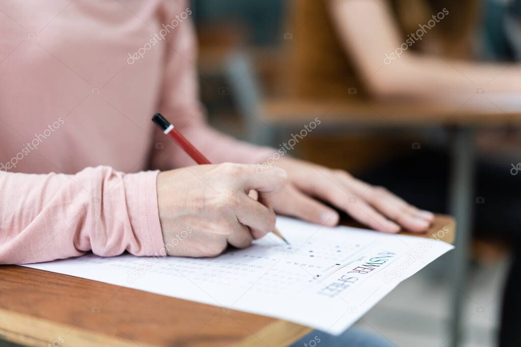 Close up of young female university students concentrate on doing examination in the classroom. Girl student writes the answer of the examinations on answer sheet in the classroom.