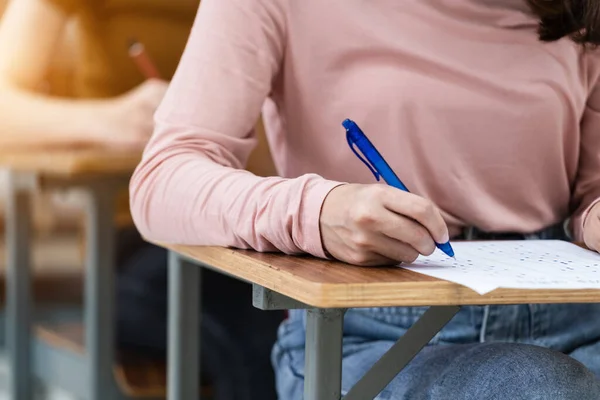 Close up of young female university students concentrate on doing examination in the classroom. Girl student writes the answer of the examinations on answer sheet in the classroom.