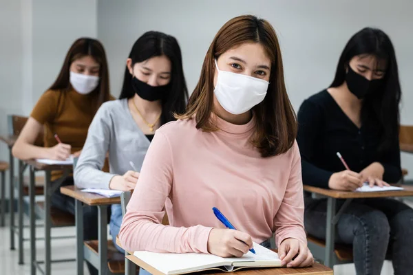 Group of college students wearing a face mask and keep distance while studying in the classroom and college or university campus to prevent COVID-19 pandemic. The new college or university campus life