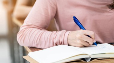 Tahta masaüstüne yerleştirilmiş not defterine yazı yazan bir kadın öğrenciyi kapat