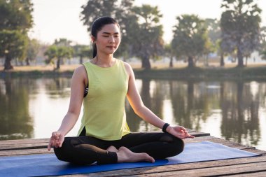Genç Asyalı güzel bir kadın nilüfer çiçeğinde yoga yapıyor ve meditasyon yapıyor. Sabahları dinlenmek ve kafa dinlemek için gölün yanında poz veriyor. Uyum ve meditasyon konsepti. Sağlıklı yaşam tarzı