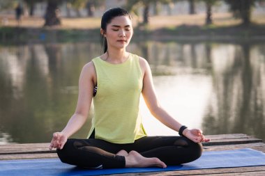 Genç Asyalı güzel bir kadın nilüfer çiçeğinde yoga yapıyor ve meditasyon yapıyor. Sabahları dinlenmek ve kafa dinlemek için gölün yanında poz veriyor. Uyum ve meditasyon konsepti. Sağlıklı yaşam tarzı