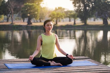 Genç Asyalı güzel bir kadın nilüfer çiçeğinde yoga yapıyor ve meditasyon yapıyor. Sabahları dinlenmek ve kafa dinlemek için gölün yanında poz veriyor. Uyum ve meditasyon konsepti. Sağlıklı yaşam tarzı