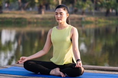 Genç Asyalı güzel bir kadın nilüfer çiçeğinde yoga yapıyor ve meditasyon yapıyor. Sabahları dinlenmek ve kafa dinlemek için gölün yanında poz veriyor. Uyum ve meditasyon konsepti. Sağlıklı yaşam tarzı