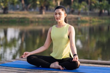 Genç Asyalı güzel bir kadın nilüfer çiçeğinde yoga yapıyor ve meditasyon yapıyor. Sabahları dinlenmek ve kafa dinlemek için gölün yanında poz veriyor. Uyum ve meditasyon konsepti. Sağlıklı yaşam tarzı