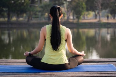 Genç Asyalı güzel bir kadın nilüfer çiçeğinde yoga yapıyor ve meditasyon yapıyor. Sabahları dinlenmek ve kafa dinlemek için gölün yanında poz veriyor. Uyum ve meditasyon konsepti. Sağlıklı yaşam tarzı