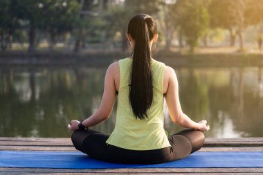 Genç Asyalı güzel bir kadın nilüfer çiçeğinde yoga yapıyor ve meditasyon yapıyor. Sabahları dinlenmek ve kafa dinlemek için gölün yanında poz veriyor. Uyum ve meditasyon konsepti. Sağlıklı yaşam tarzı