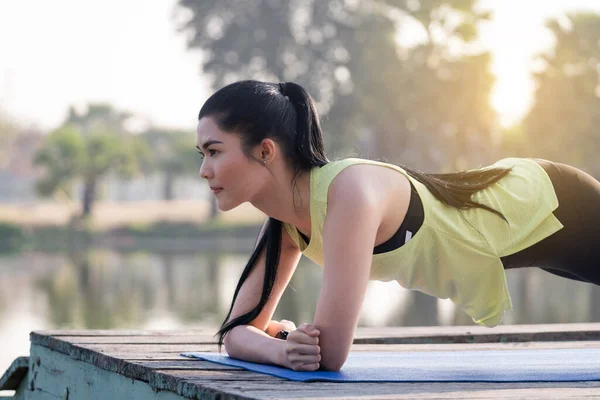 Young beautiful Asian woman in sports outfits planking in the park in the morning to practice balance and strength to get a healthy lifestyle. Young beautiful athletic woman doing a plank exercise.