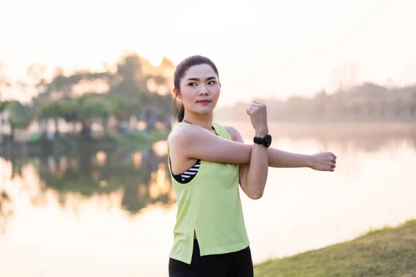 Young beautiful Asian woman in sports outfits doing stretching before workout outdoor in the park in the morning to get a healthy lifestyle. Healthy young woman warming up outdoors. Sport and Recreation