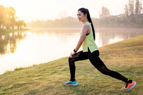 Young Asian female workout before fitness training session at the park under sunlight in the morning. Healthy young woman warming up outdoors. Sport and recreation