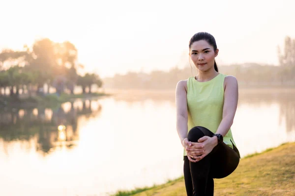 Young Asian female workout before fitness training session at the park under sunlight in the morning. Healthy young woman warming up outdoors. Sport and recreation