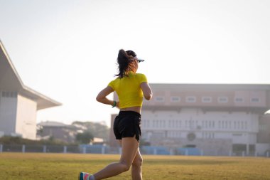 Genç bir Asyalı bayan atlet, formda ve sağlıklı yaşam tarzını korumak için güneşli bir sabahta şehir stadyumunda koşu pistinde koşuyor. Genç fitness kadını stadyum pistinde koşuyor. Spor ve eğlence.