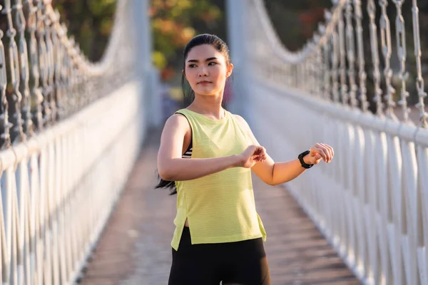 A young Asian woman runner athlete in sports outfit doing stretching and warm up before workout, jogging and fitness training session in the city park in the morning. Sports and recreation
