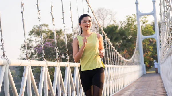 A young Asian woman athlete runner jogging in city stadium in the sunny morning to keep fitness and healthy lifestyle. Active healthy runner jogging outdoor. Sports and recreation