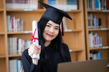 Genç bir Asyalı bayan üniversite mezunu, mezuniyetini kutlamak için sevinç ve heyecan dolu bir şekilde bir dizüstü bilgisayarın önünde ailesine uzaktan bir video konuşması yapıyor.