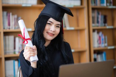 Genç bir Asyalı bayan üniversite mezunu, mezuniyetini kutlamak için sevinç ve heyecan dolu bir şekilde bir dizüstü bilgisayarın önünde ailesine uzaktan bir video konuşması yapıyor.