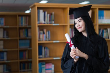 Mezuniyet elbisesi ve maske takan mutlu bir Asyalı kadın üniversitesi mezuniyet törenindeki başarısını kutlamak için diploma tutuyor. Stok fotoğrafı