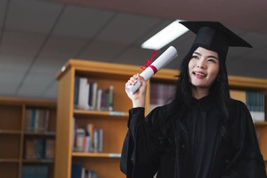Mezuniyet elbisesi ve maske takan mutlu bir Asyalı kadın üniversitesi mezuniyet törenindeki başarısını kutlamak için diploma tutuyor. Stok fotoğrafı