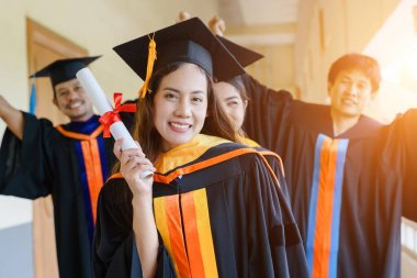 Üniversite mezuniyet elbisesi ve havan topu şapkasıyla mezuniyet töreninde elde eğitim başarısını kutlamak için diploma alır. Mezuniyetleri kutlarım.