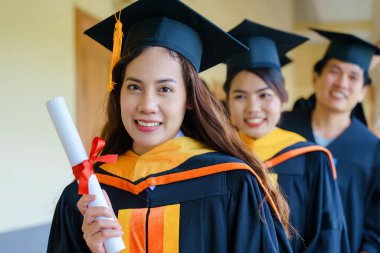 Üniversite mezuniyet elbisesi ve havan topu şapkasıyla mezuniyet töreninde elde eğitim başarısını kutlamak için diploma alır. Mezuniyetleri kutlarım.