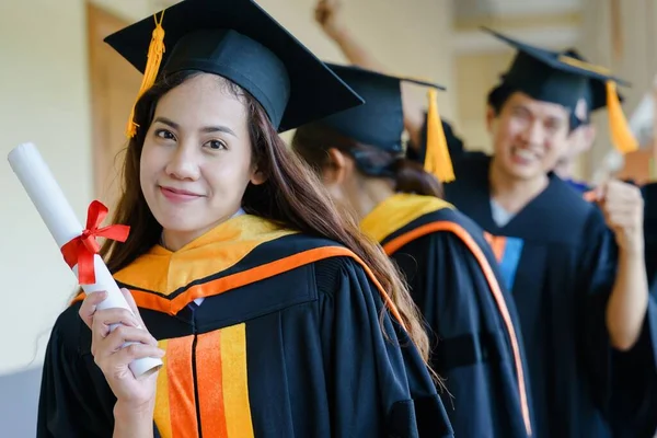 Üniversite mezuniyet elbisesi ve havan topu şapkasıyla mezuniyet töreninde elde eğitim başarısını kutlamak için diploma alır. Mezuniyetleri kutlarım.