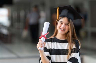 Genç Asyalı kadın üniversite mezunları mezuniyet elbisesi ve havan tahtasının üniversite kampüsünde eğitim başarısını kutlamak için diploması var. Eğitim stoku fotoğrafı