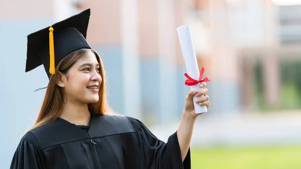 一名身穿毕业礼服的年轻快乐的亚洲女大学生在大学校园里获得了学位证书 以庆祝她的教育成就 教育库存照片 — 图库照片