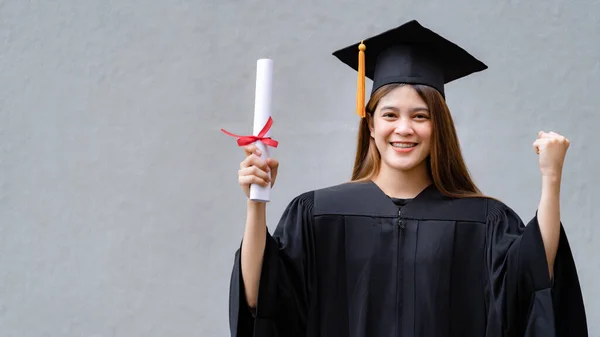 卒業生のガウンとモーターボードを着た若い幸せなアジアの女性大学卒業生は 大学のキャンパスで教育の成果を祝う学位証明書を保持しています 教育ストックフォト — ストック写真