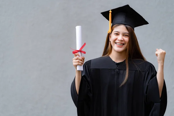 卒業生のガウンとモーターボードを着た若い幸せなアジアの女性大学卒業生は 大学のキャンパスで教育の成果を祝う学位証明書を保持しています 教育ストックフォト — ストック写真