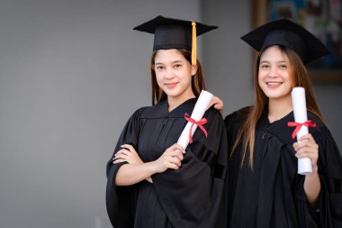 Genç mutlu Asyalı kadın üniversite mezunları mezuniyet elbisesi ve havan tahtasıyla üniversite kampüsünde eğitim başarısını diploma ile kutluyorlar. Eğitim stoku fotoğrafı