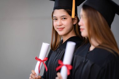 Genç mutlu Asyalı kadın üniversite mezunları mezuniyet elbisesi ve havan tahtasıyla üniversite kampüsünde eğitim başarısını diploma ile kutluyorlar. Eğitim stoku fotoğrafı