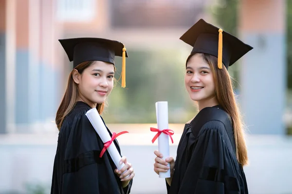 若い幸せなアジアの女性の大学卒業生は卒業生のガウンとモルタルボードは 大学のキャンパスで教育の成果を祝う学位証明書を保持します 教育ストックフォト — ストック写真