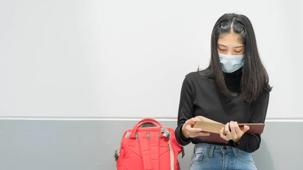 A young Asian woman college student wears a medical face mask with a school backpack to protect from influenza virus COVID-19 pandemic while studying in college building campus. Education stock photo