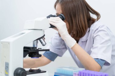 Laboratuvarda araştırma ve deney yapmak için mikroskoptan bakan laboratuvar önlüklü genç bir bilim kadını. Laboratuvarda çalışan bir bilim adamı. Eğitim stoku fotoğrafı