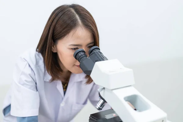 A young scientist woman in a laboratory coat looking through a microscope in a laboratory to do research and experiment. Scientist working in a laboratory. Education stock photo