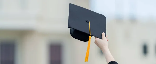 Mezuniyet elbisesi ve havan tahtasıyla güzel bir Asyalı kadın üniversite mezunu üniversite mezuniyetine katıldıktan sonra üniversite binasının önünde diploma tutuyor.