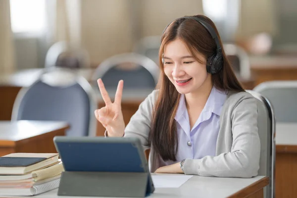 Young interactive happy Asian teenage girl university student studying and presenting her lesson online via video call on a digital tablet in the classroom alone herself. Education stock photo