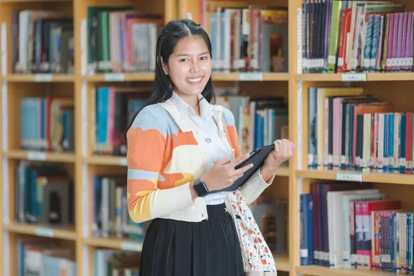 大学図書館や大学図書館でスマートかつ幸せなポーズでタブレットを保持制服を着た若いアジアの女性学生 女子学生と技術学習コンセプトで教育を指導 — ストック写真