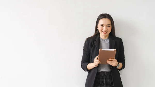 ビジネススーツ姿の明るいアジアの実業家が ビジネスビルのデジタルタブレットを使って立っている姿を描いています 業務用ストックフォト — ストック写真