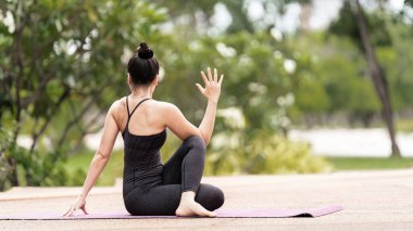Spor kıyafetli orta yaşlı, kendinden emin bir Asyalı kadın sabahları arka bahçede yoga minderinde yoga egzersizi yapıyor. Genç bir kadın doğa parkında yoga egzersizi yapıyor.