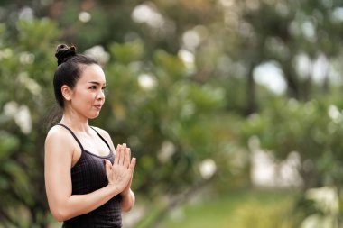 Spor kıyafetli orta yaşlı, kendinden emin bir Asyalı kadın sabahları arka bahçede yoga minderinde yoga egzersizi yapıyor. Genç bir kadın doğa parkında yoga egzersizi yapıyor.