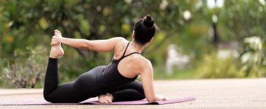 Spor kıyafetli orta yaşlı, kendinden emin bir Asyalı kadın sabahları arka bahçede yoga minderinde yoga egzersizi yapıyor. Genç bir kadın doğa parkında yoga egzersizi yapıyor.